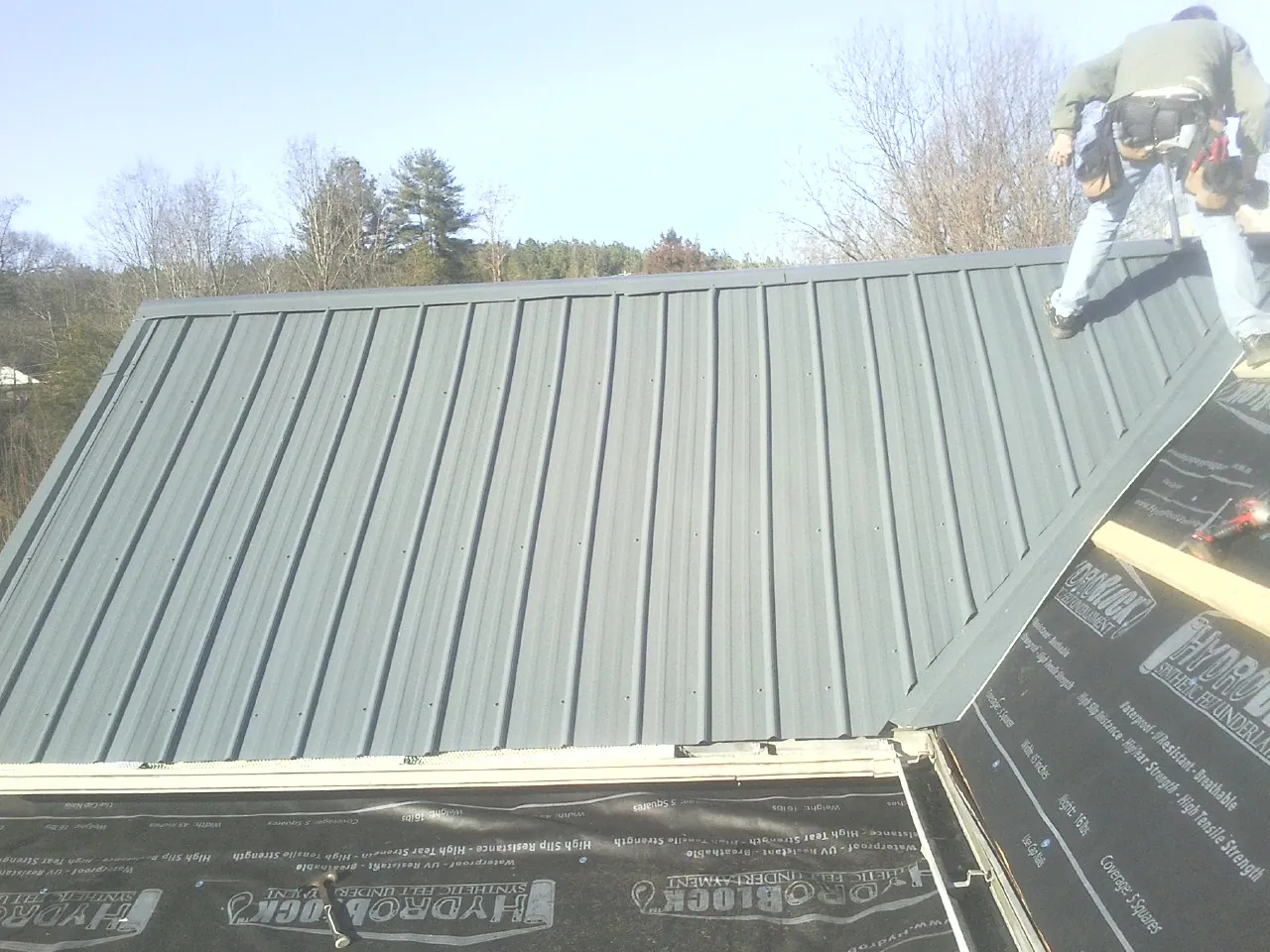 Crew installing dark green standing seam panels over synthetic underlayment in Newton