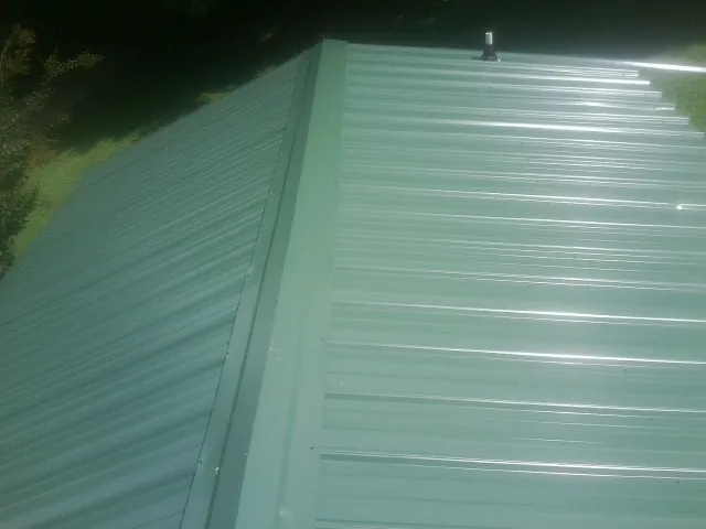 New green metal panels meeting at the ridge of a roof — Flat Roof Repair work by our crew in Newton